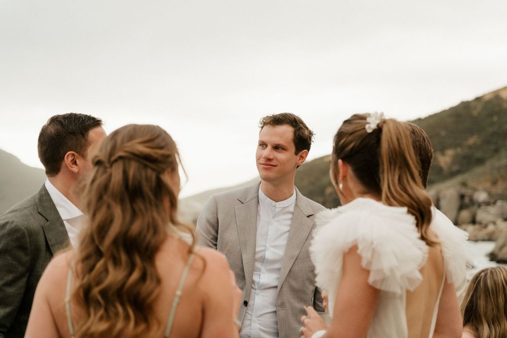 Intimate wedding gathering with guests conversing outdoors against mountain scenery.