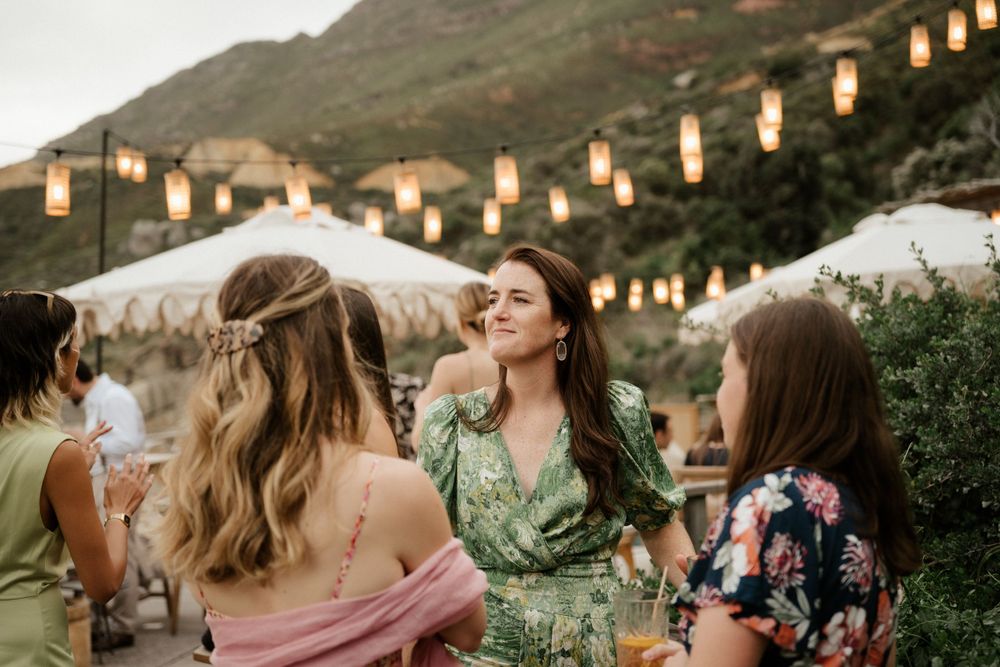 Wedding guests enjoying an outdoor reception with hanging lanterns and mountain backdrop at sunset.