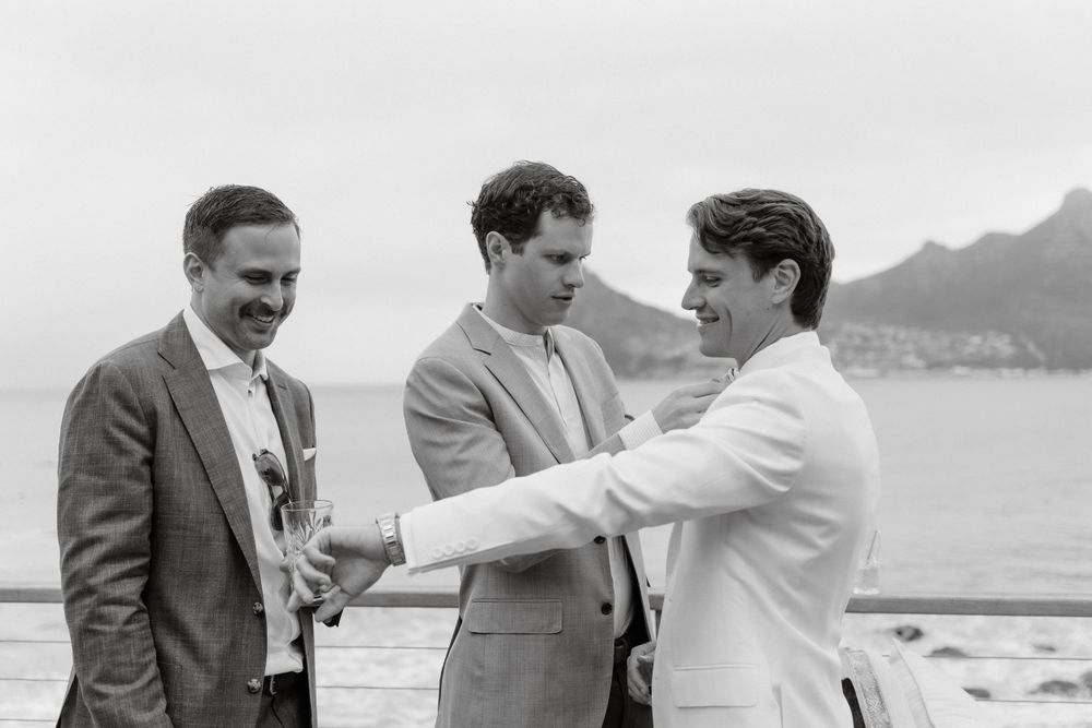 Three formally dressed people share a joyful moment together by the ocean.