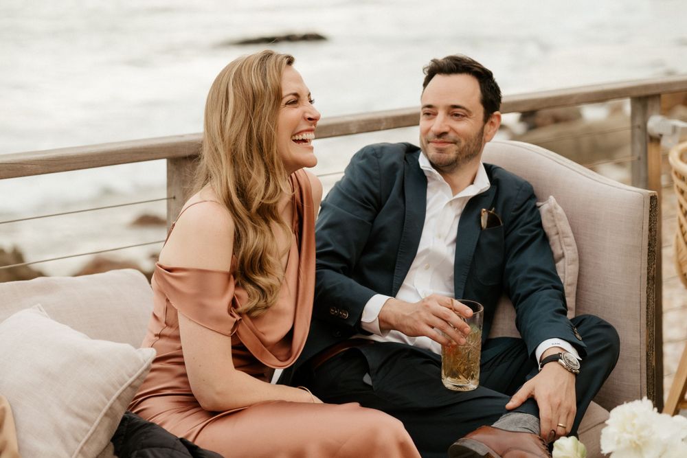 Couple sharing drinks and laughter on outdoor patio seating.
