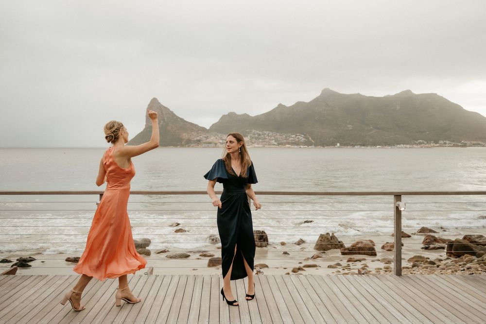 Two people dance together on a wooden deck overlooking a dramatic coastal landscape.