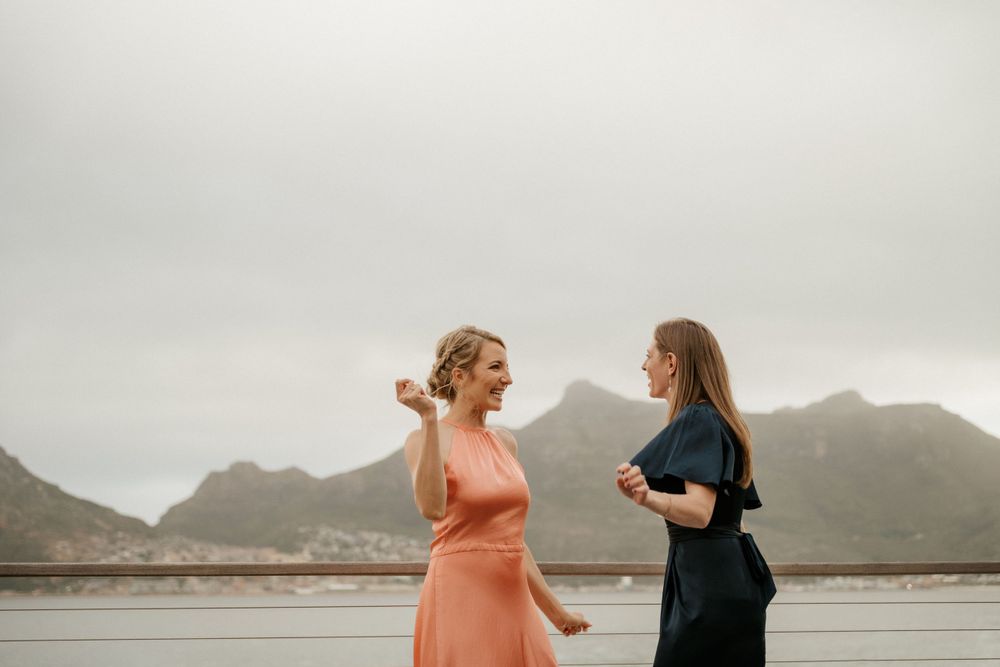 Two women laughing and dancing on a deck overlooking mountain scenery.