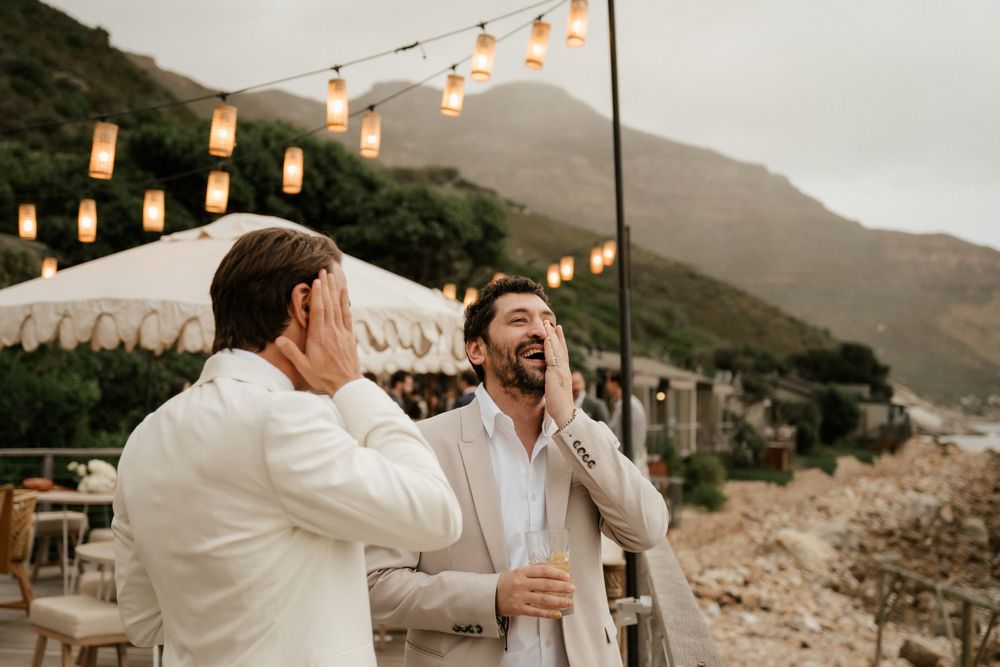 Two guests sharing laughs under string lights at outdoor evening reception.