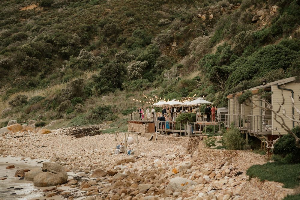 Rustic beach setting with wooden structures and umbrellas along a rocky coastline.