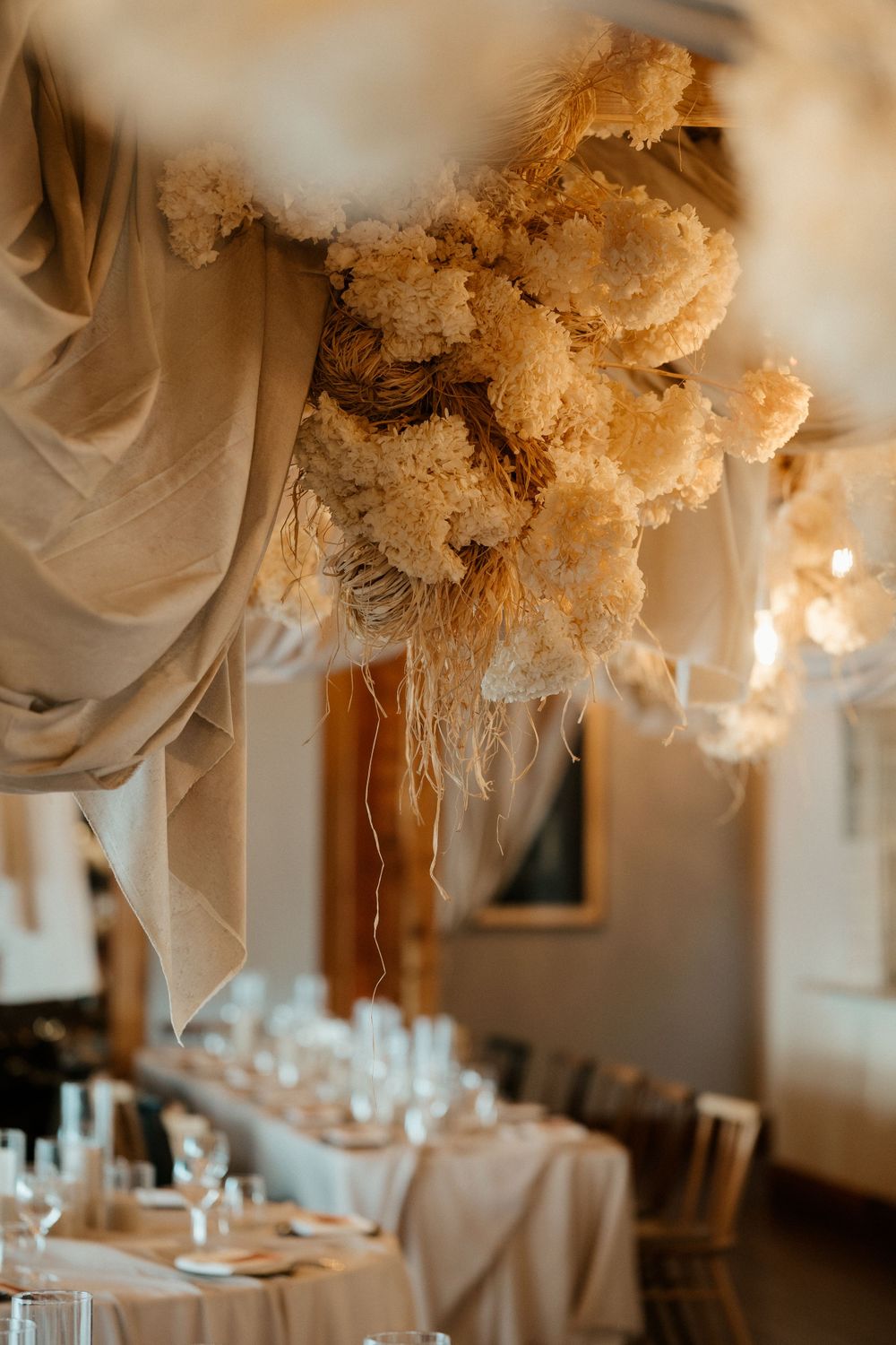 Elegant wedding reception table setting with dramatic floral ceiling installation and soft drapery.