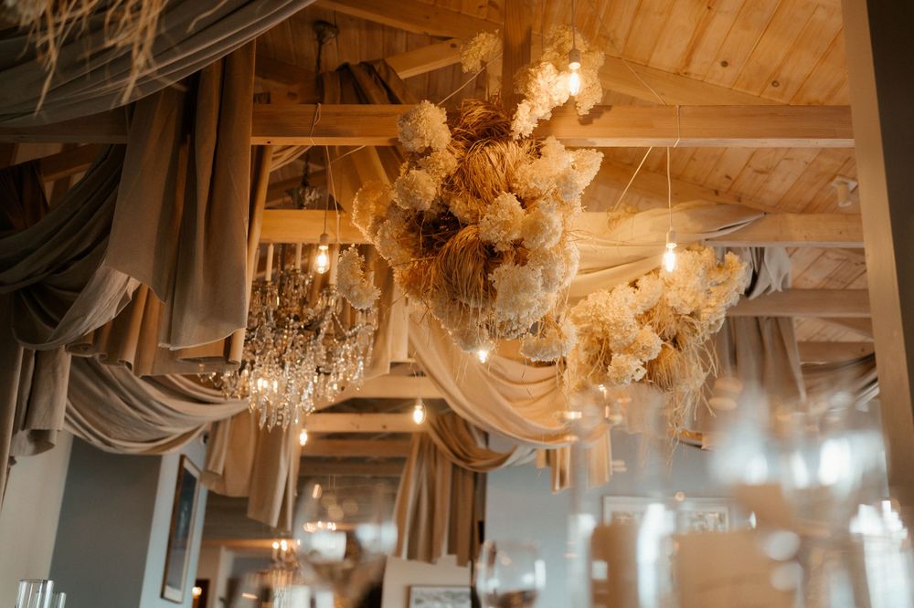 Elegant chandelier and draped fabric decor in a rustic wooden ceiling reception venue.