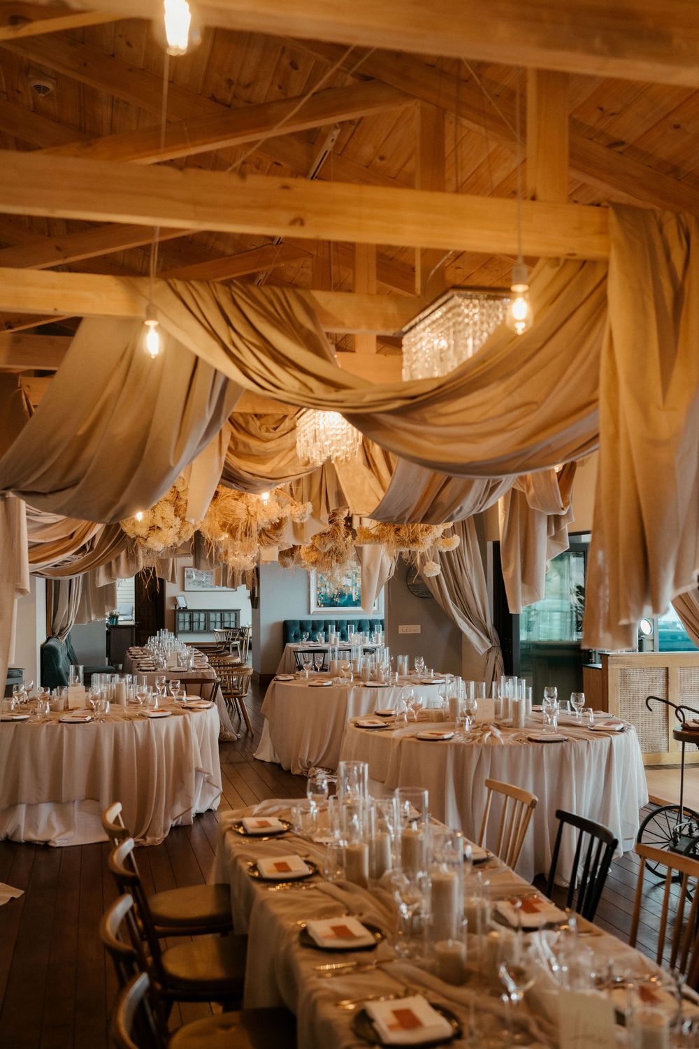 Elegant wedding reception venue with draped fabric ceiling, crystal chandeliers, and round tables set for dining.