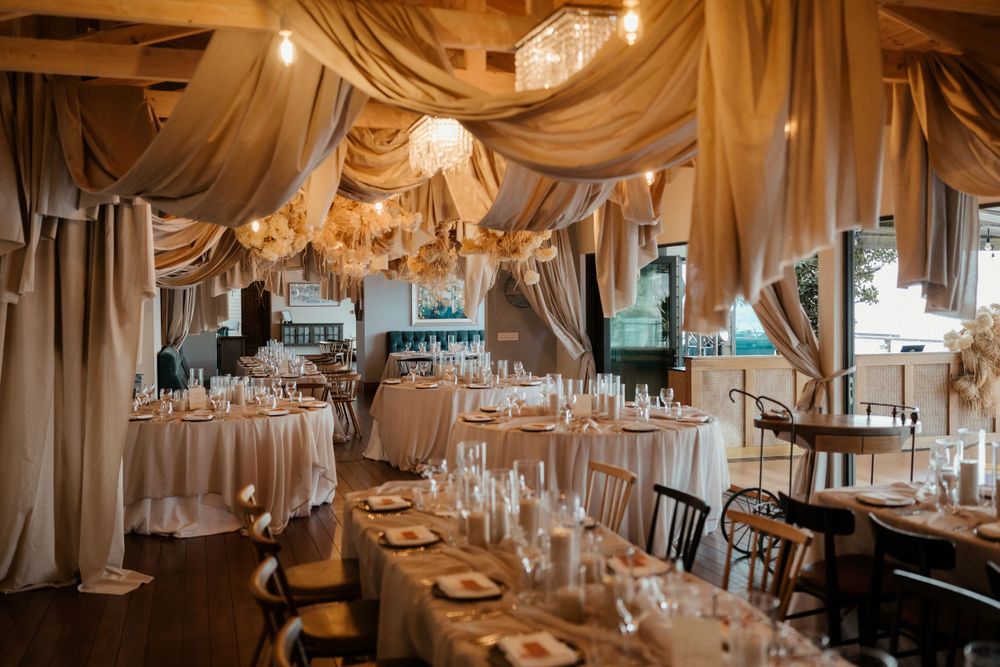 Elegant wedding reception venue with draped fabric ceiling and crystal chandeliers over round tables.