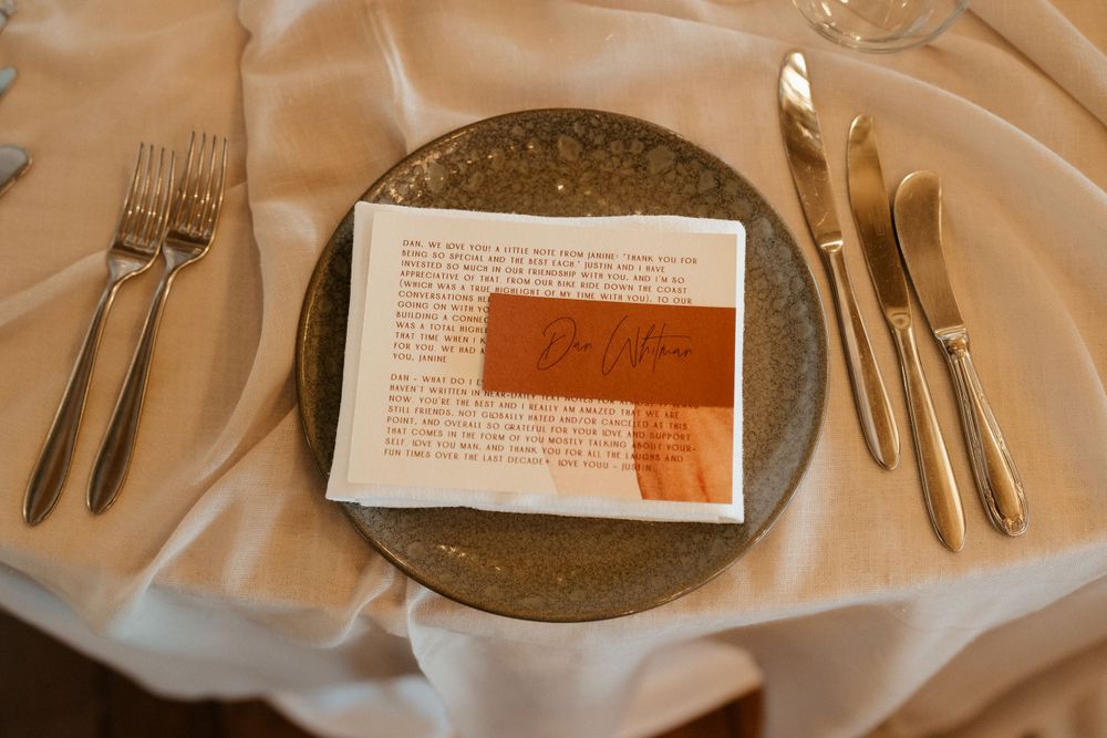 Place setting with handwritten note card and gold cutlery on textured plate.
