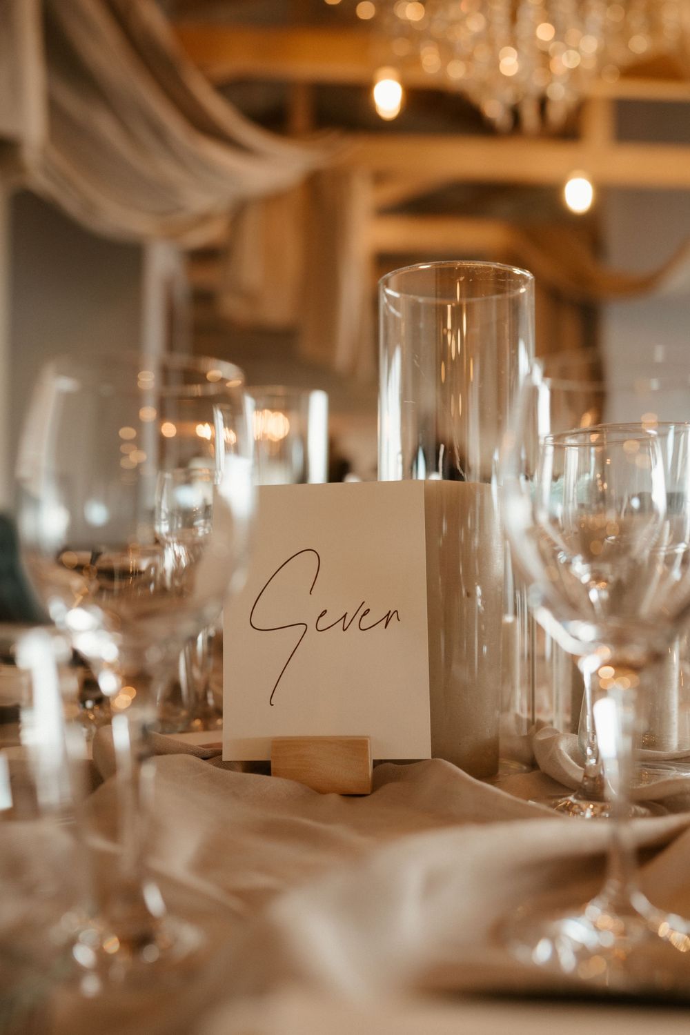 Elegant table setting with 'Seven' table number card and crystal glassware for wedding reception.
