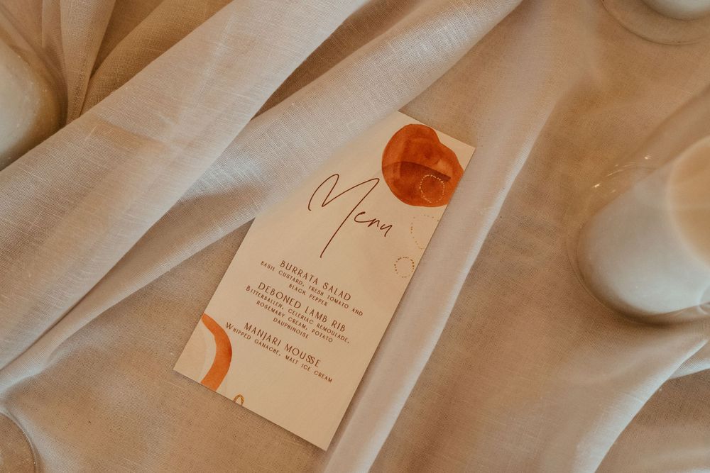 Wedding menu card with orange wax seal on soft fabric backdrop.