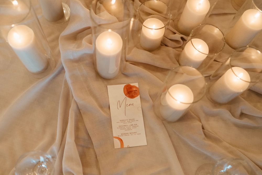 Wedding decor with glowing candles and name card on cream fabric.