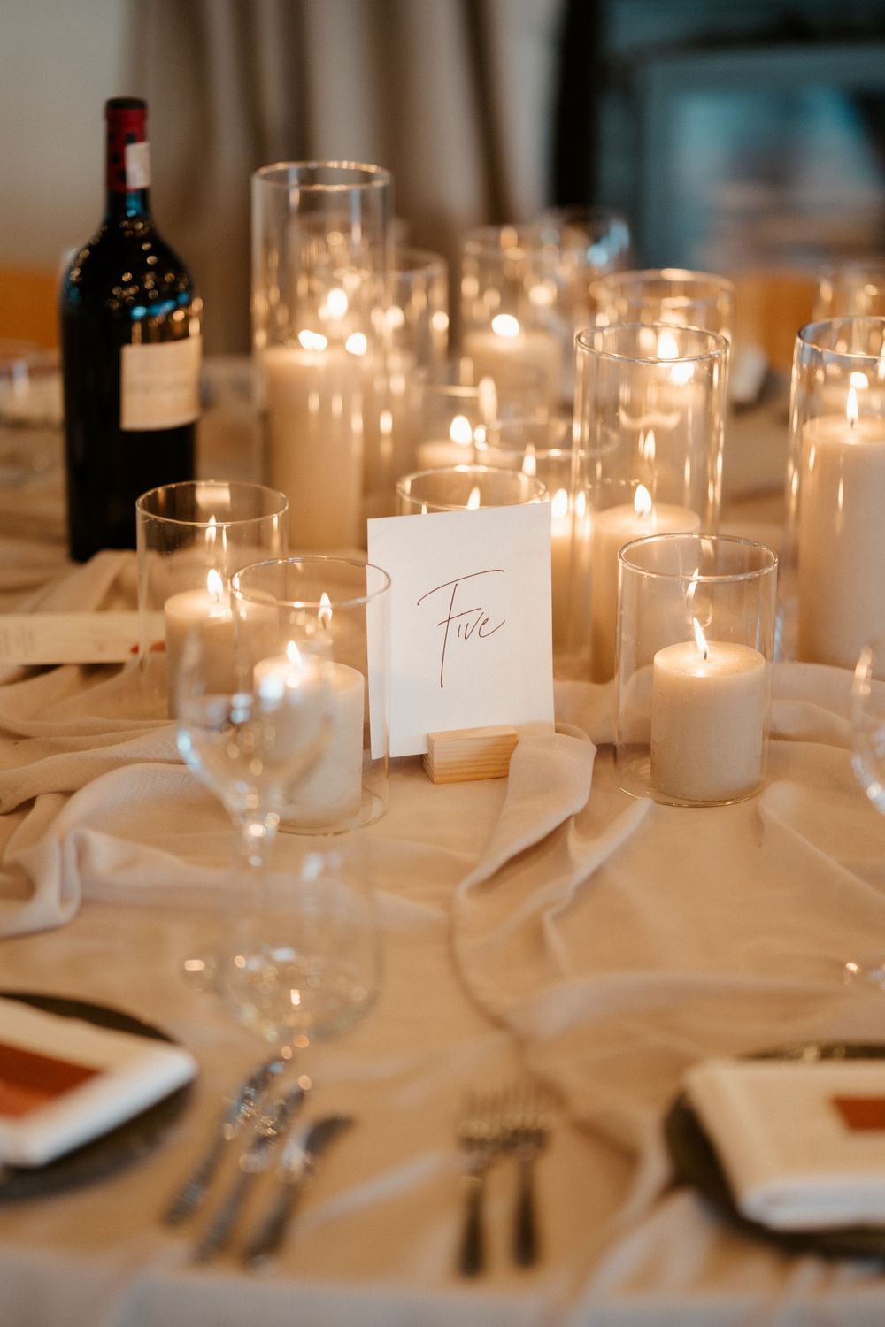 Elegant table setting with glowing candles and wine bottles for a wedding reception.