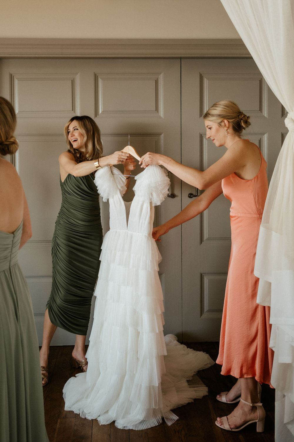 Bridesmaids in elegant dresses helping with a white wedding gown before the ceremony.