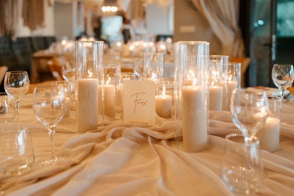 Elegant wedding reception table setting with white candles, wine glasses and champagne-colored linens.