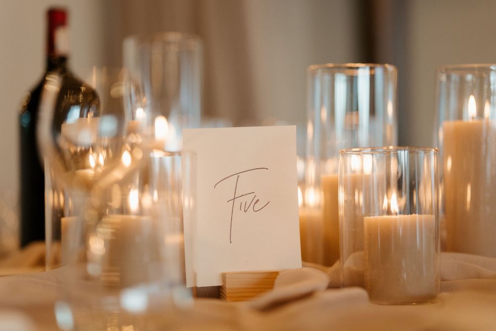 Elegant table setting with candles and 'Five' table number card at wedding reception.