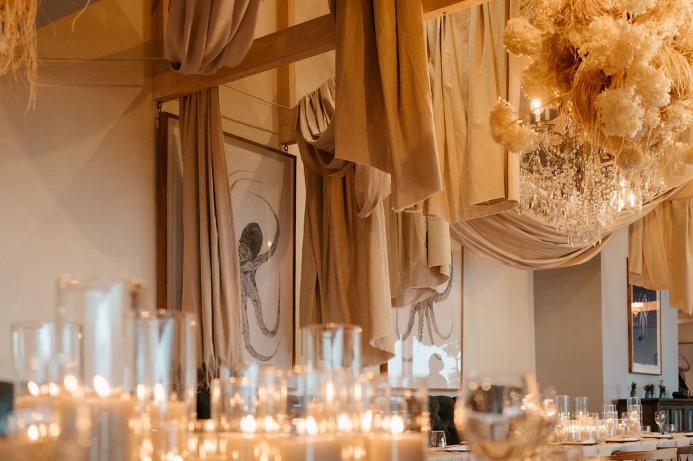 Elegant wedding reception table setting with candles and chandeliers in a draped ballroom.
