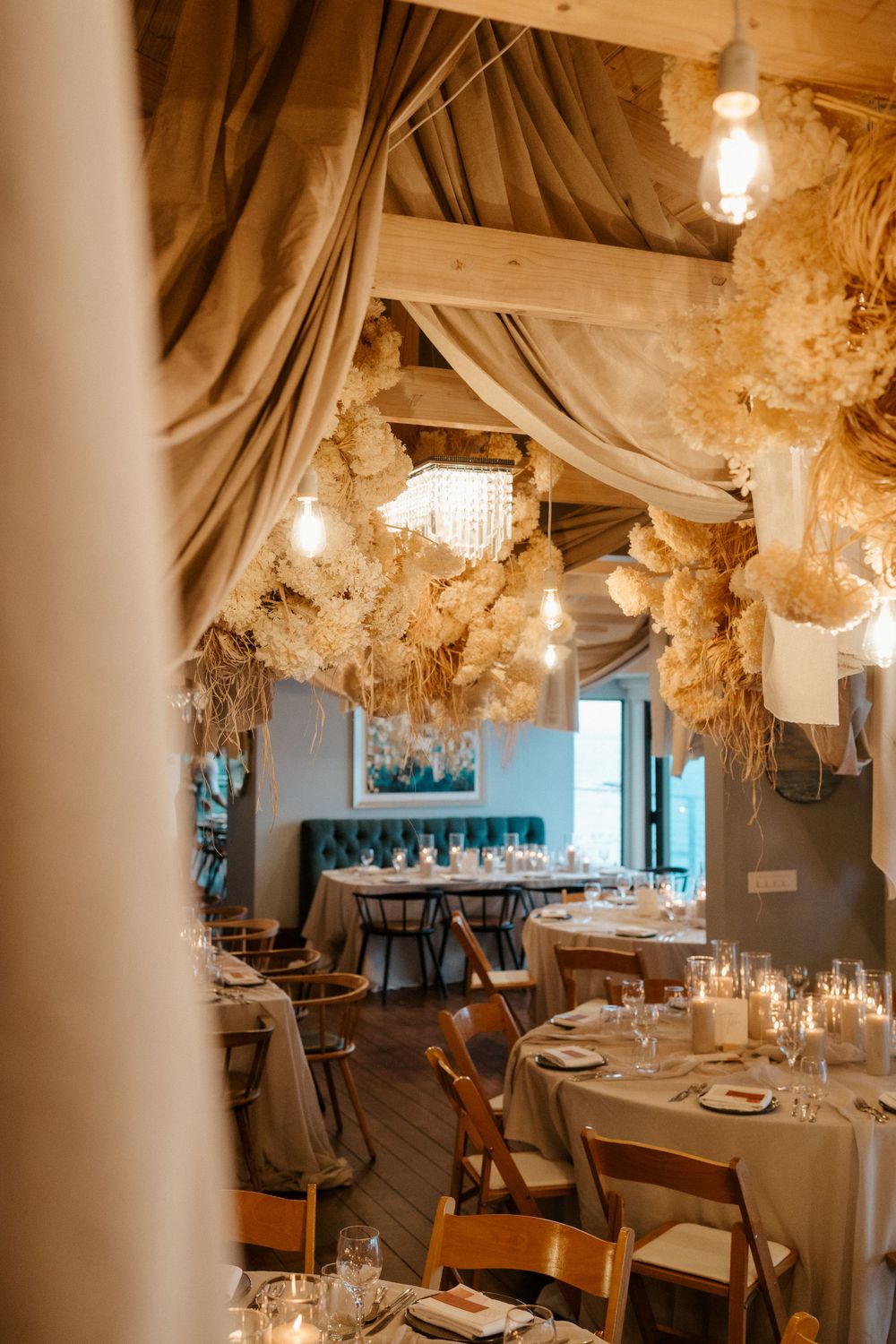Romantic restaurant interior with draped fabric ceiling, crystal chandeliers, and intimate table settings on wooden floors.