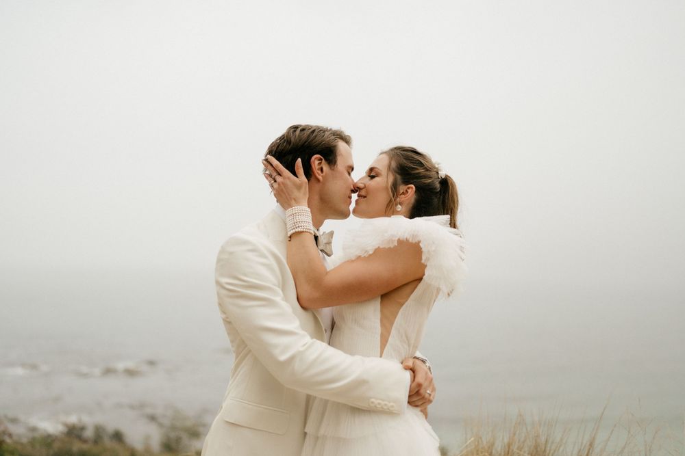 Romantic foggy coastal wedding portrait of couple embracing in formal attire.