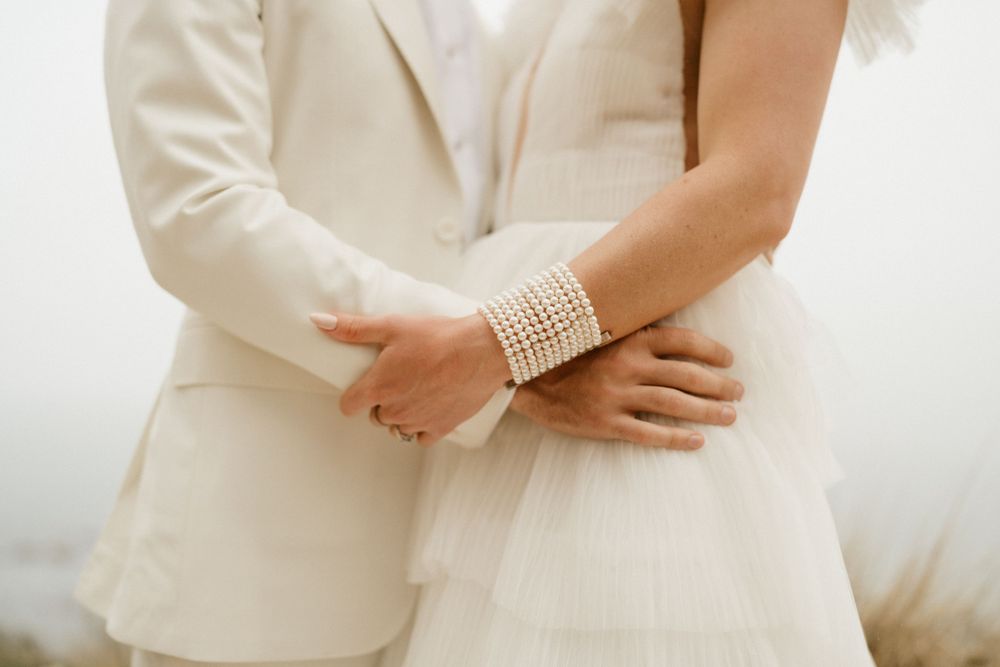 Close-up detail of couple embracing showing pearl bracelet and cream colored formal wear.