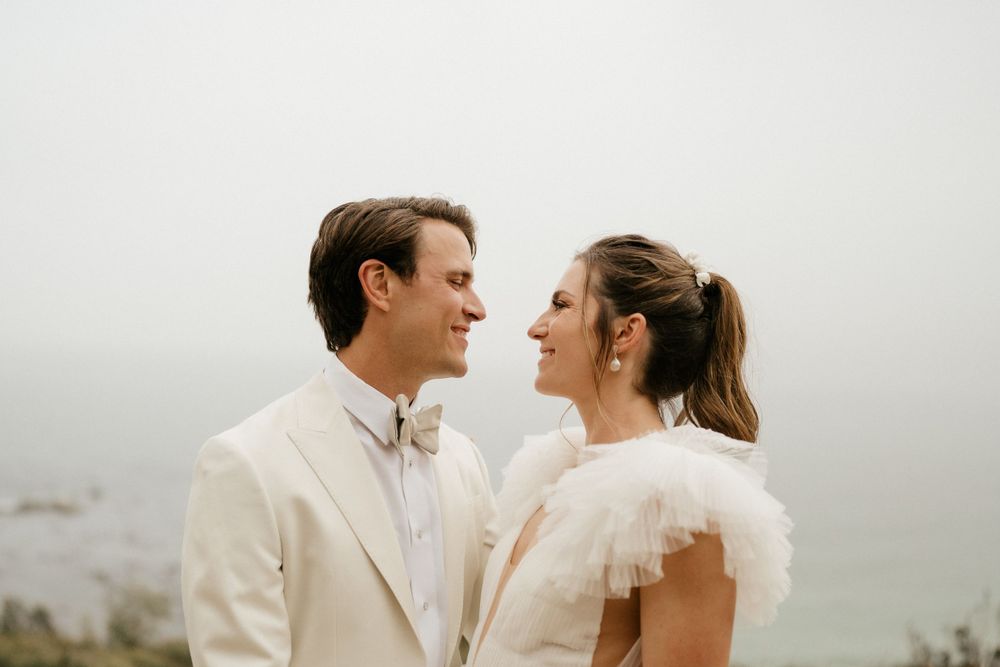 Couple in white wedding attire sharing intimate moment against misty background.