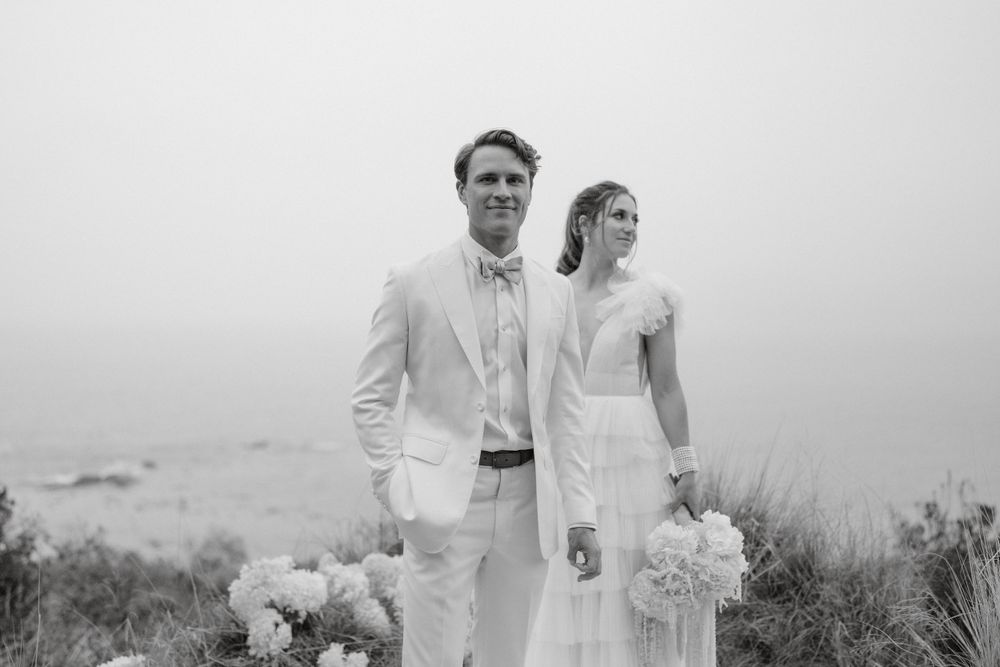 A romantic coastal wedding portrait with a couple in light attire against a misty backdrop.