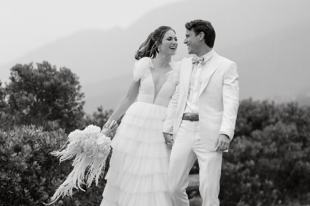 Black and white portrait of couple in wedding attire laughing together outdoors.