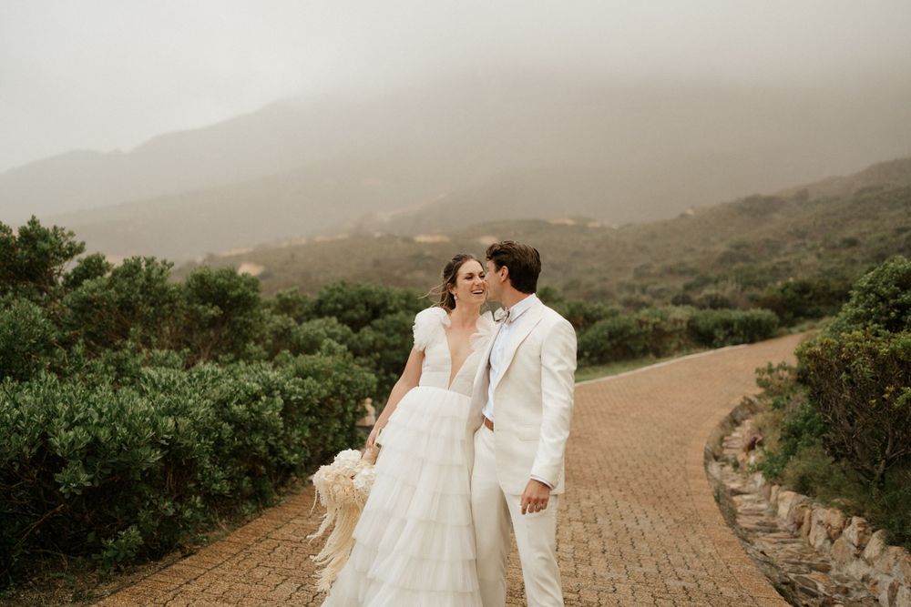 Couple in wedding attire walking along winding mountain path.