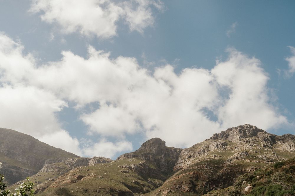 Rugged mountain peaks rise against a bright blue sky with white puffy clouds.