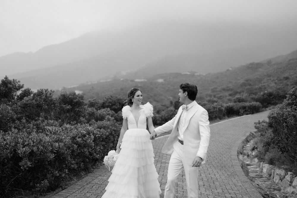 Black and white photo of newlyweds walking together on a winding mountain path.