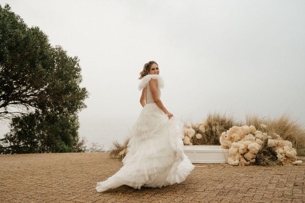 Bride in flowing white dress twirls on stone path with mountain landscape behind.
