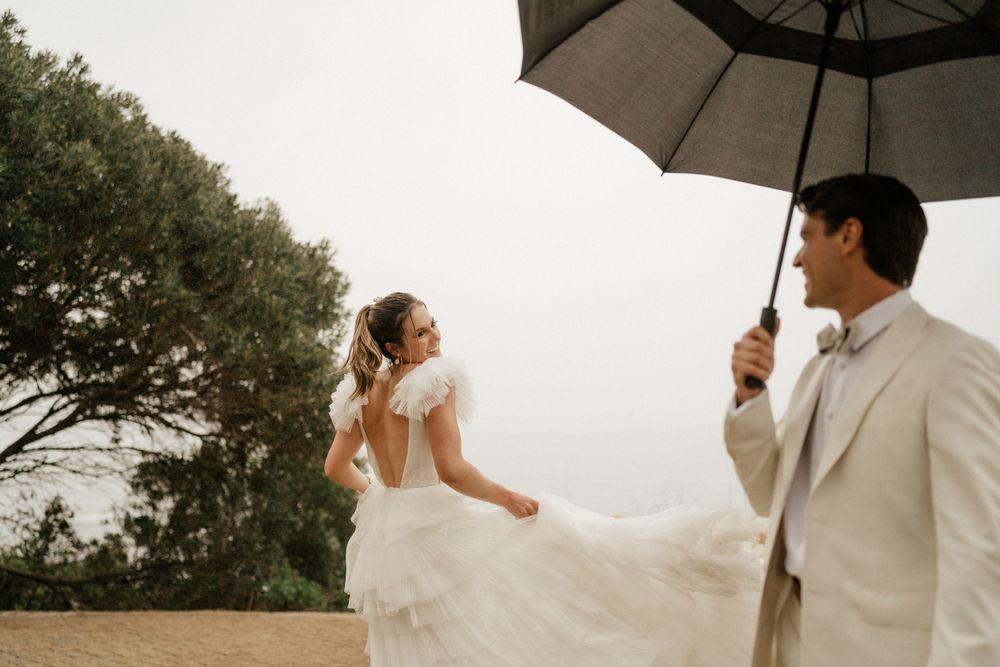 Couple sharing playful moment with umbrella during coastal wedding photoshoot.