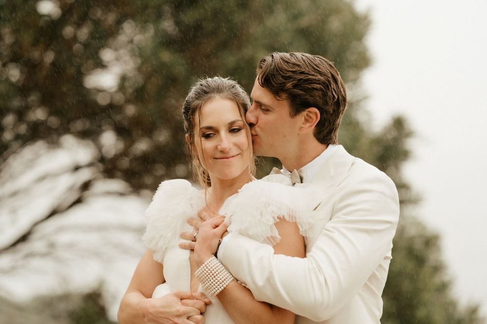Intimate wedding portrait captured against soft cloudy sky and natural backdrop.