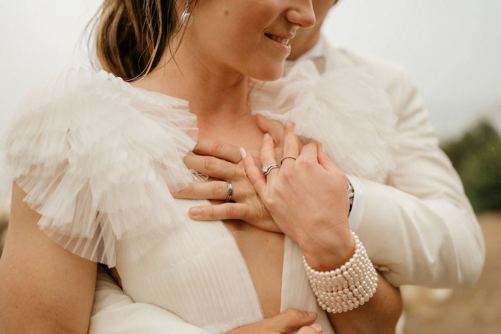 Close-up of pearl bracelet and wedding ring details with ruffle dress sleeve.