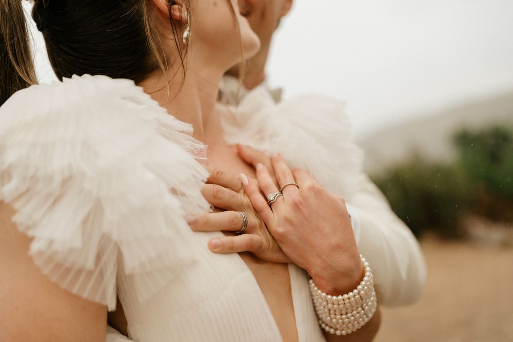 Close-up view of pearl bracelet and engagement ring on a white ruffled dress sleeve.