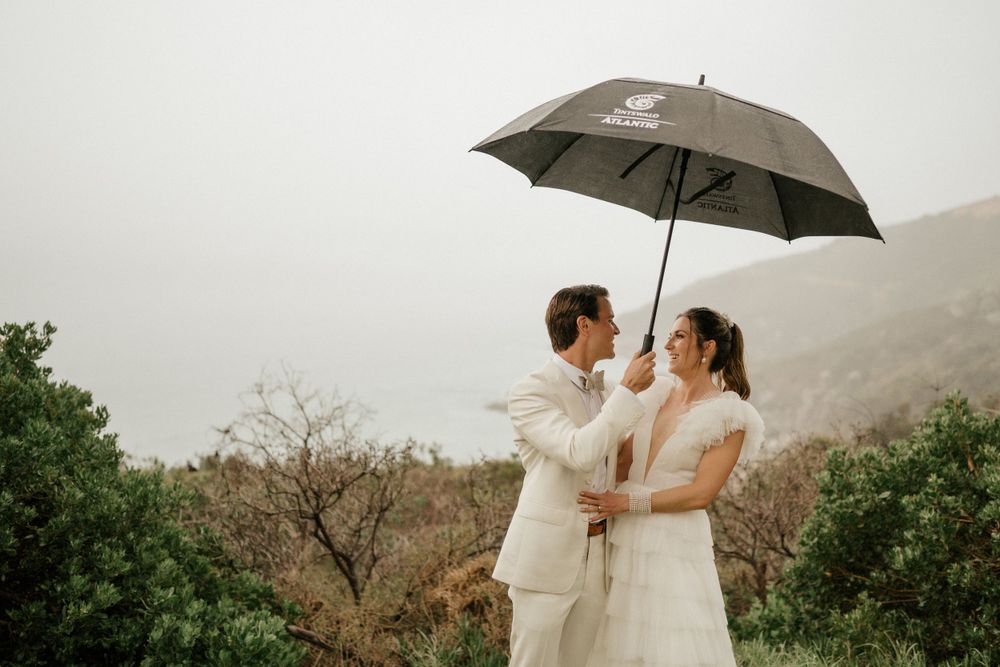 Couple sharing intimate moment under umbrella with misty mountain backdrop.