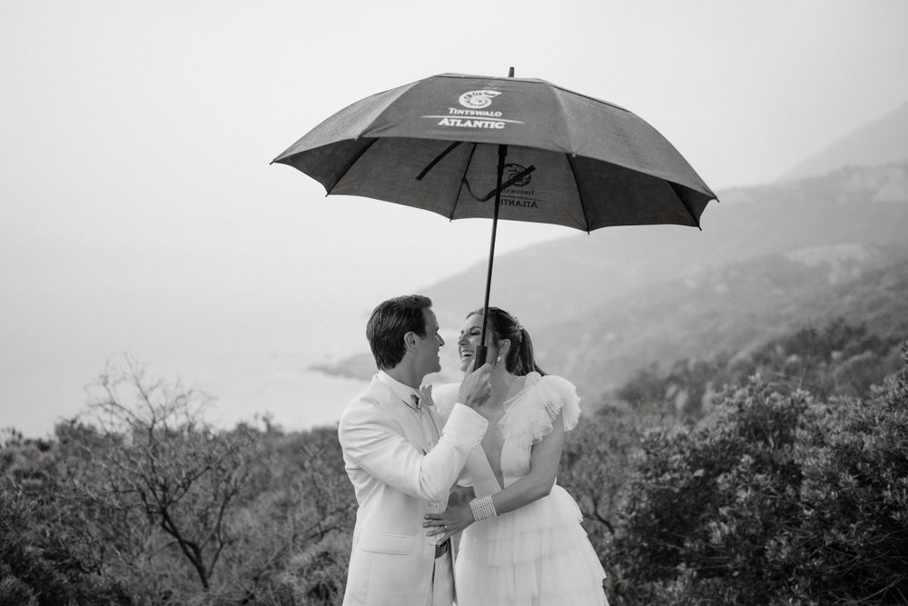 Romantic black and white portrait of couple sharing umbrella in mountain landscape.