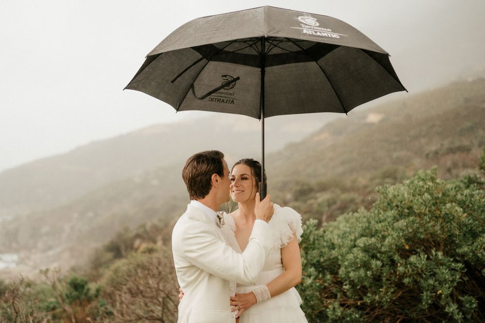 Romantic couple shares intimate moment under grey umbrella on misty hillside.