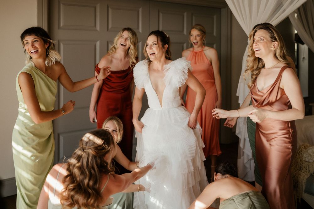 Bridesmaids in silk dresses of varying colors help with wedding preparations.