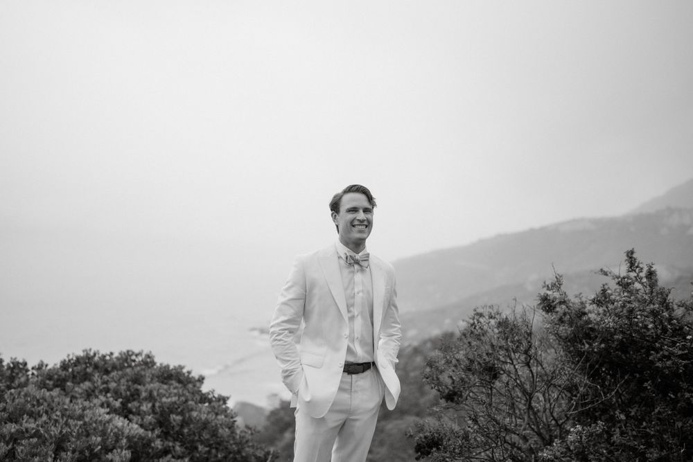 Person in white suit poses against misty mountain landscape.