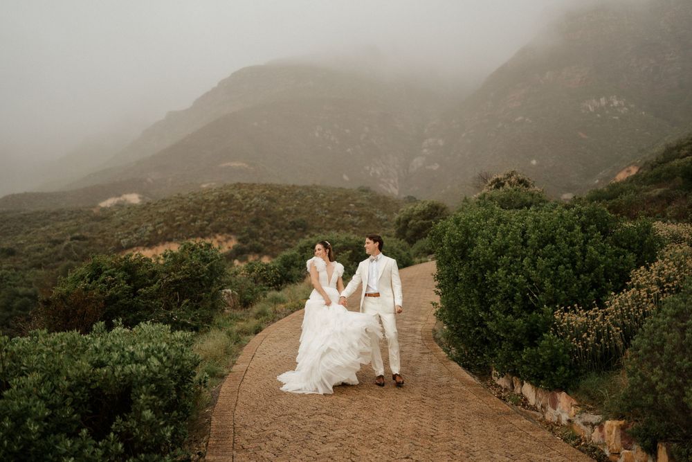 Couple walks along a misty mountain path in formal wedding attire during their scenic outdoor photoshoot.
