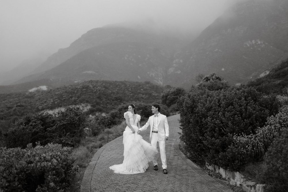 A romantic black and white photo of newlyweds walking down a misty mountain path.