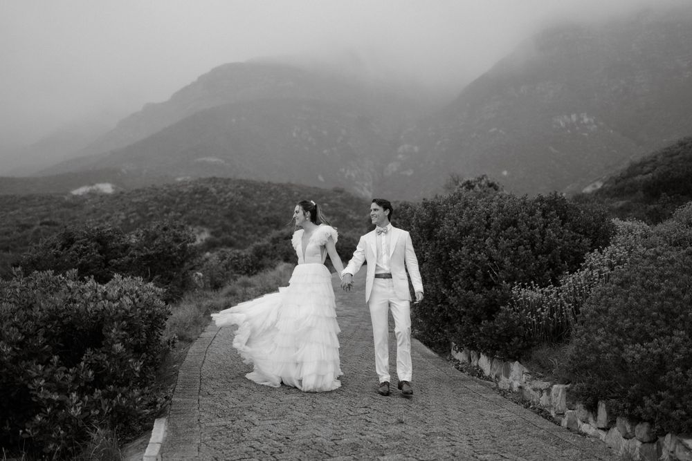 Black and white photo of a couple walking on a mountain trail in wedding attire.
