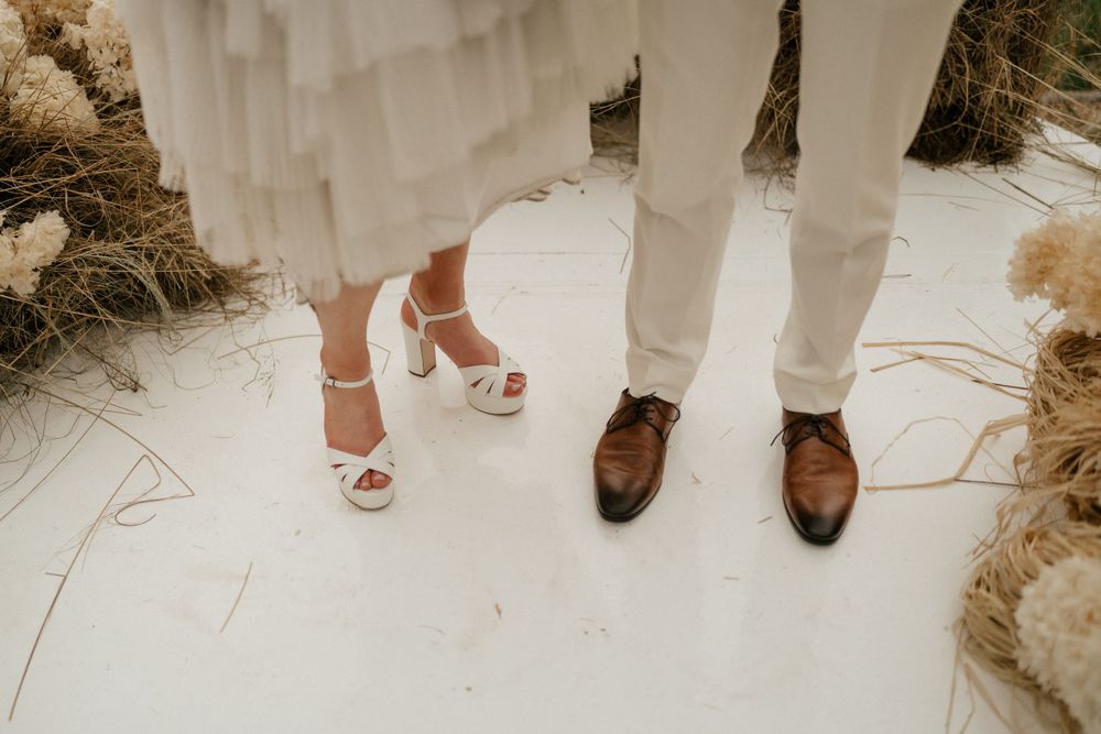 Wedding couple's feet showing elegant heels and dress shoes on white surface.
