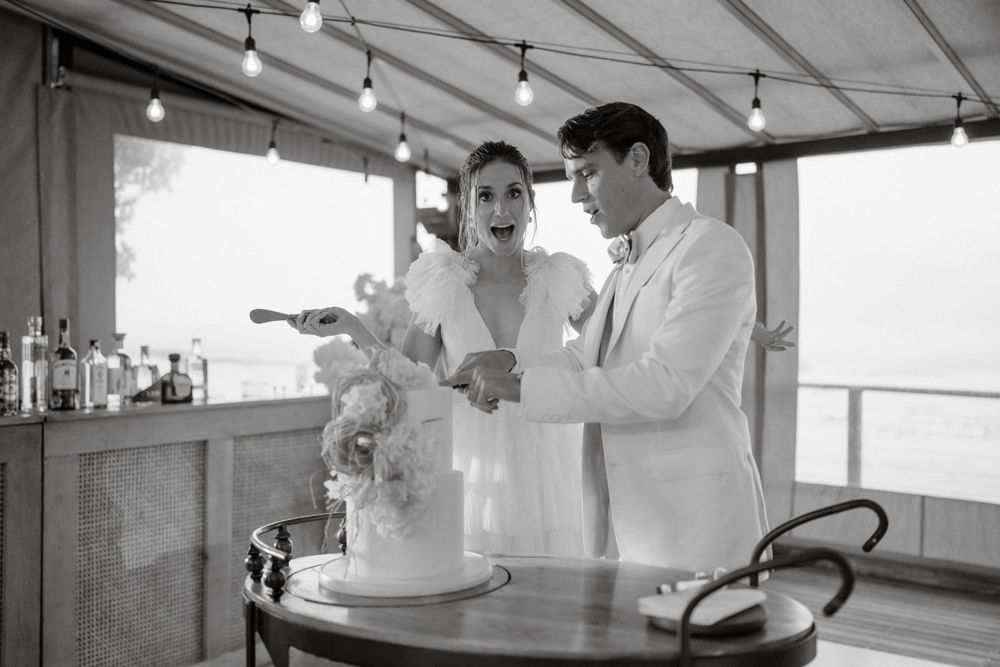 Black and white photo of a wedding cake cutting moment at an outdoor covered venue.