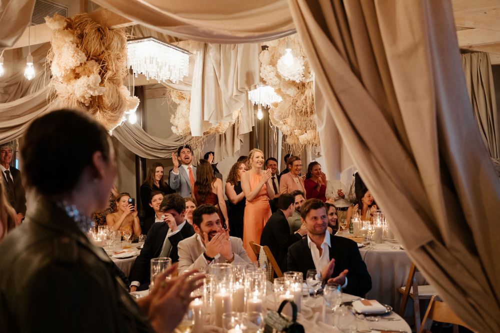 Guests seated at candlelit tables during an elegant wedding reception under flowing white fabric drapes.