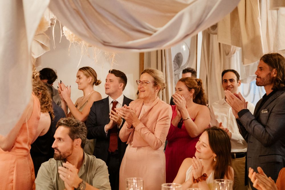 Wedding guests applaud during indoor reception with draped fabric decor.