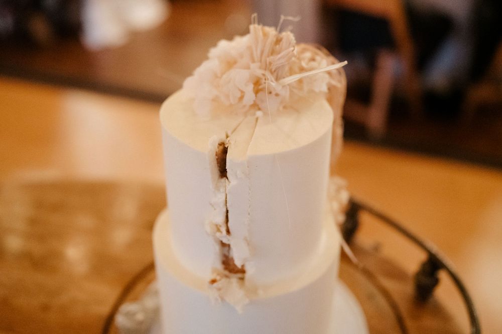 A white tiered wedding cake with delicate floral details displayed on a wooden table.