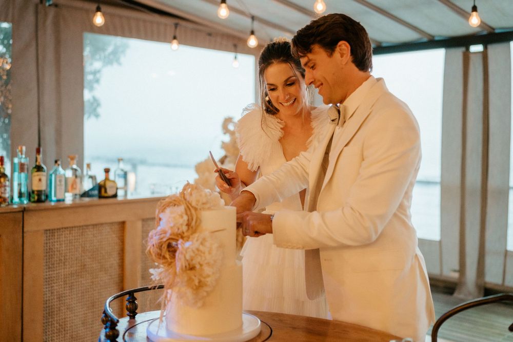 Newlyweds share a happy moment while cutting their wedding cake together at an indoor reception.