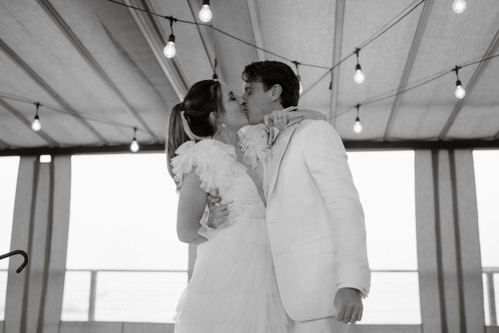 A tender wedding day kiss shared under string lights and draped fabric.
